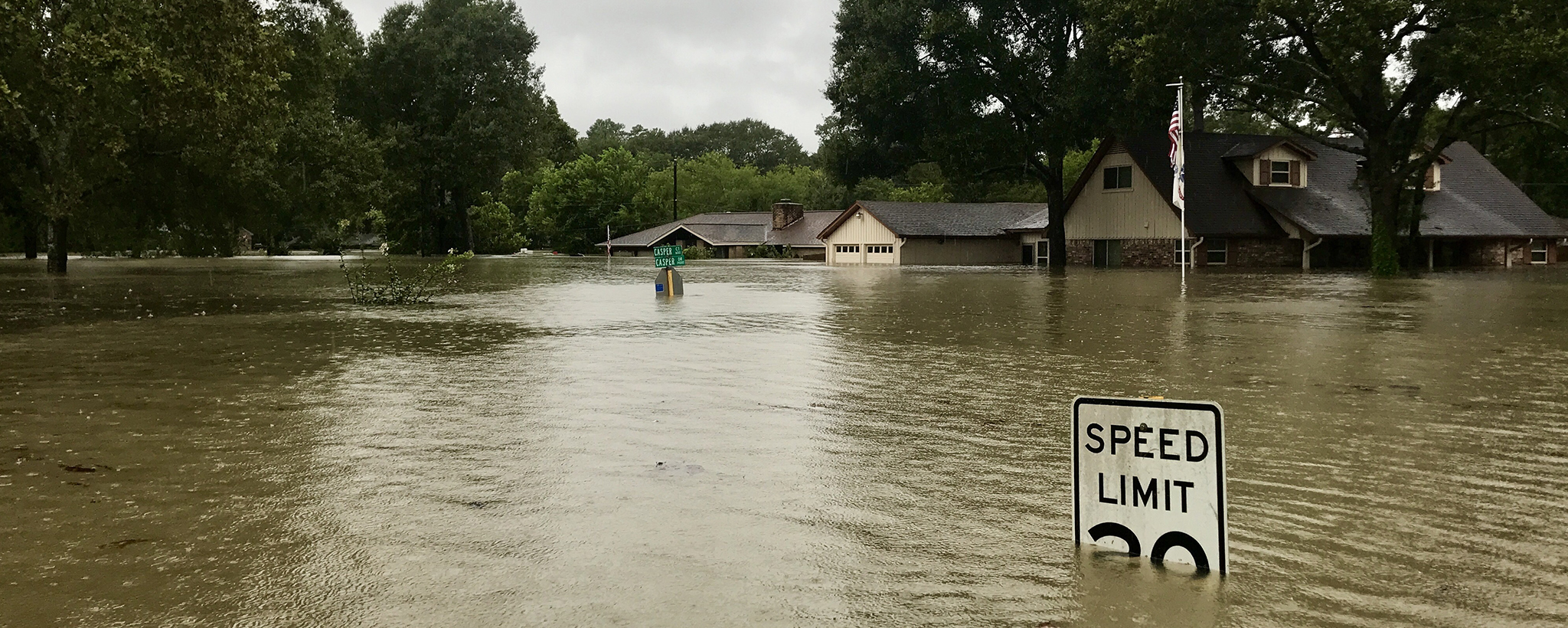 Flooded neighborhood. Flood waters cover a speed limit sign, houses in the background.